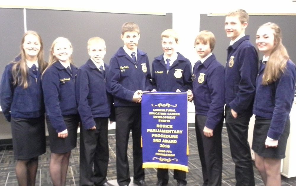 Edon-FFA-3rd-in-State---PHOTO PROVIDED WEB - The Village Reporter Proudly displaying their Third Place Award Banner (the first-ever accomplishment in parliamentary procedure for Edon FFA) are 2015-2016 Novice Parli Pro team members, from left: Riley Bloir, Secretary; Claire Radabaugh, Member; Cameron Siebenaler, Student Advisor; Shane Zulch, Vice President; Aidan Muehlfeld, President; Tatum Schaffter, Treasurer; Connor Skiles, Sentinel and Alea Brandt, Reporter. The team was coached by Hannah Everetts, Edon FFA Chapter Advisor.