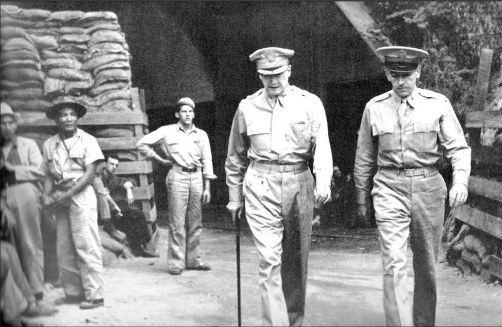 Four starred General MacArthur and two starred Chief of Staff, General Sutherland, step briskly out of the main enterance to the Corregidor Tunnels. To the left with his hand upon his hip is Junior Wyse.