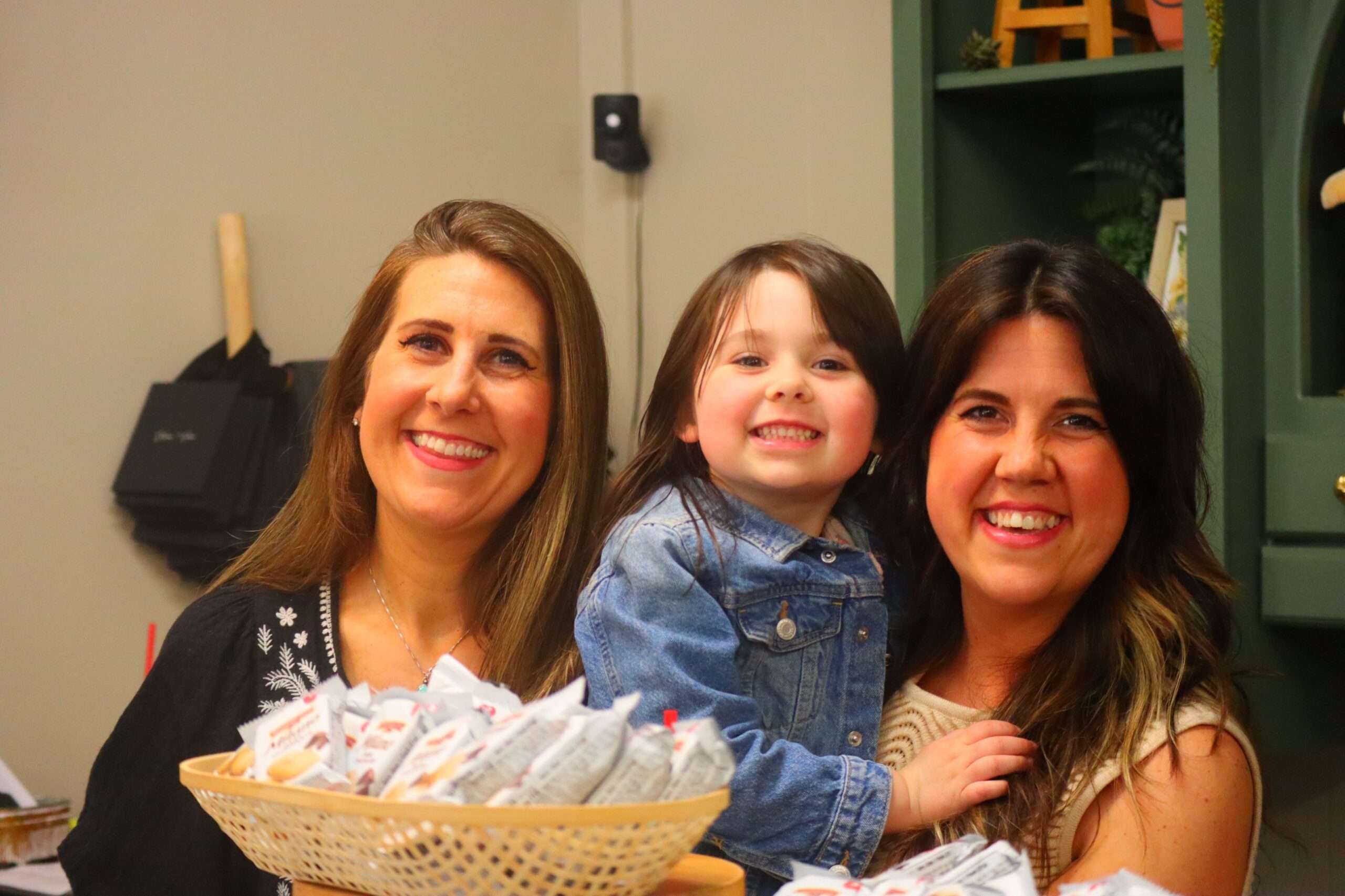 Two women holding a small child between them, with a basket of chocolate samples in front, inside Silver and Vine during the Bryan Chocolate Walk.