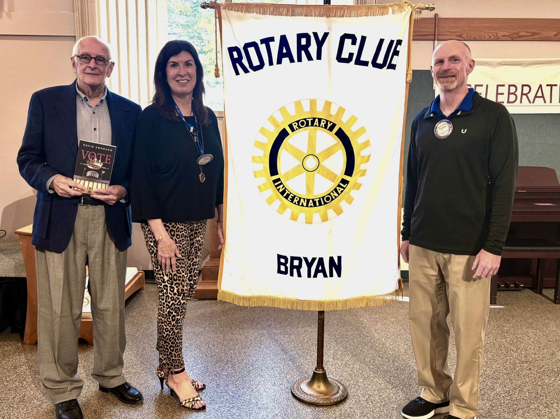 Author David Swanson with Rotarians Jenny Horn and Tyson Moss in front of the Bryan Rotary banner