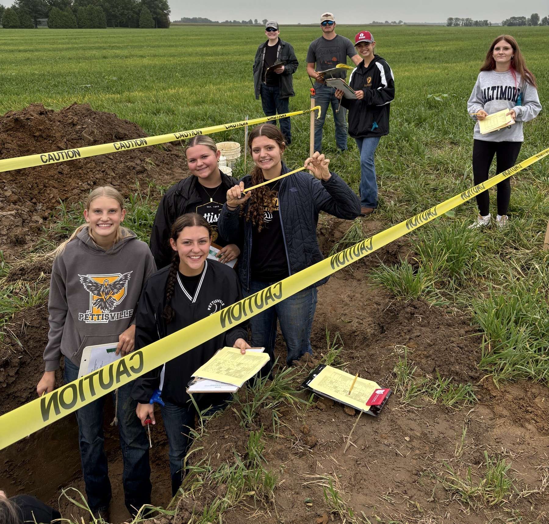 Eight Pettisville FFA members around a soil pit with caution tape in a field