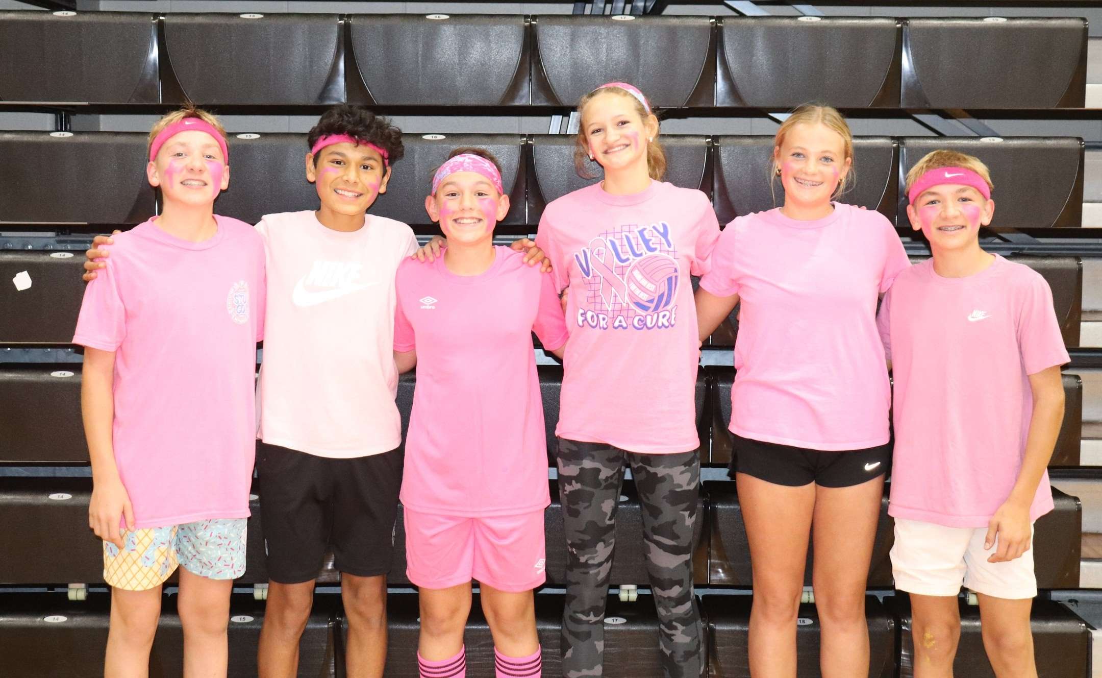Six junior high dodgeball winners in pink shirts and headbands in the bleachers