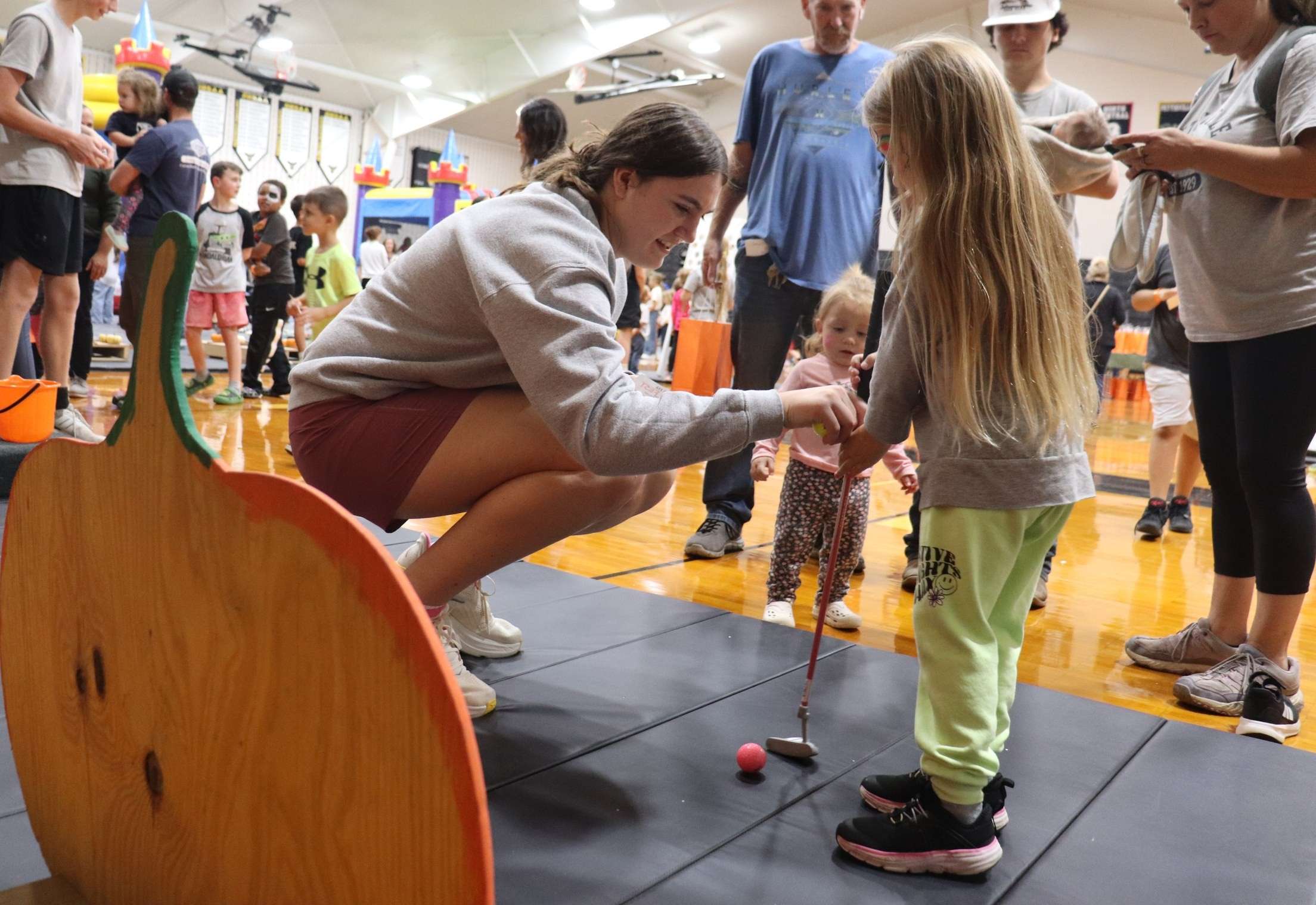 Lucy Mendoza helping a young girl with putt-putt at the kids game area