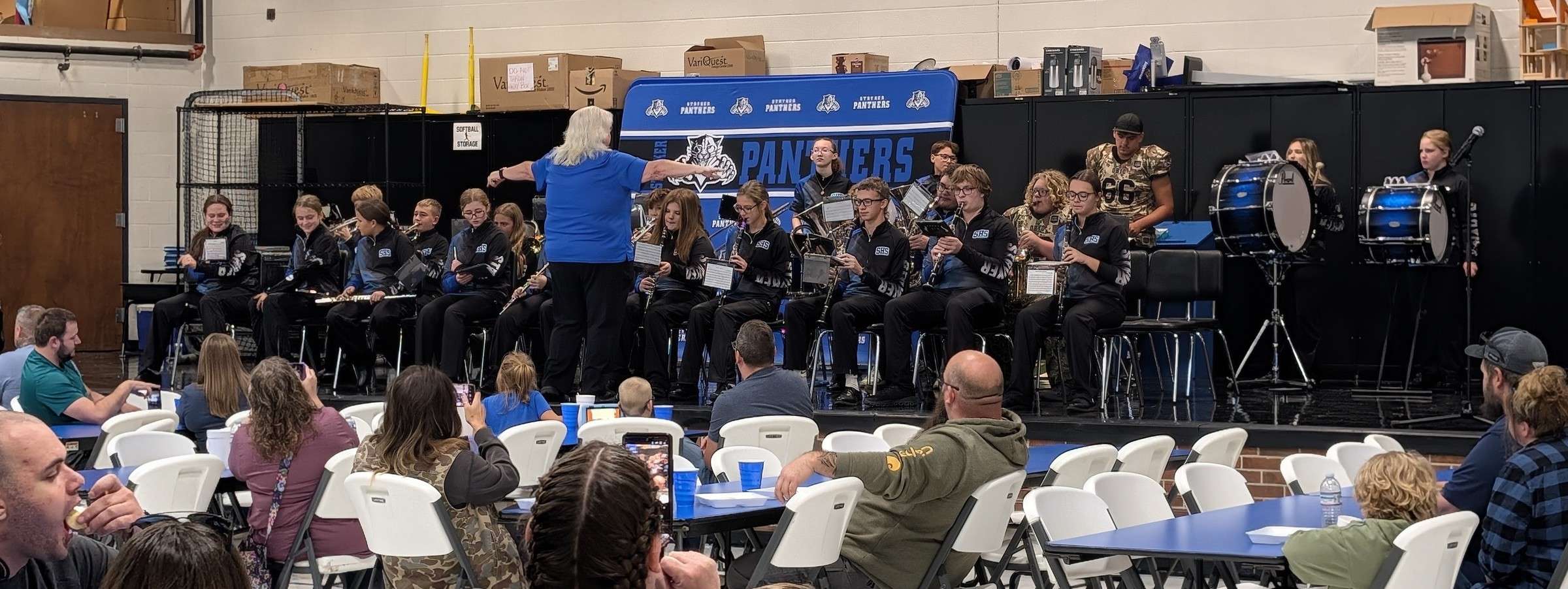 Stryker band members in black jackets on a stage with a conductor while families watch from tables