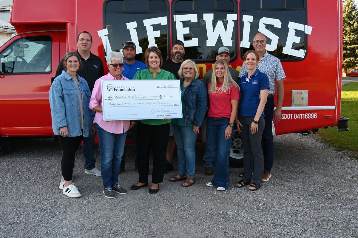 Edon Area Foundation members and grant recipients hold a $31,100 check in front of a LifeWise bus