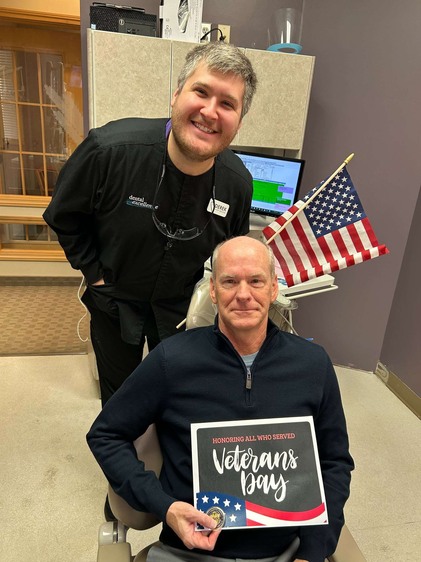 Dental Excellence dentist with a veteran patient holding a Veterans Day sign