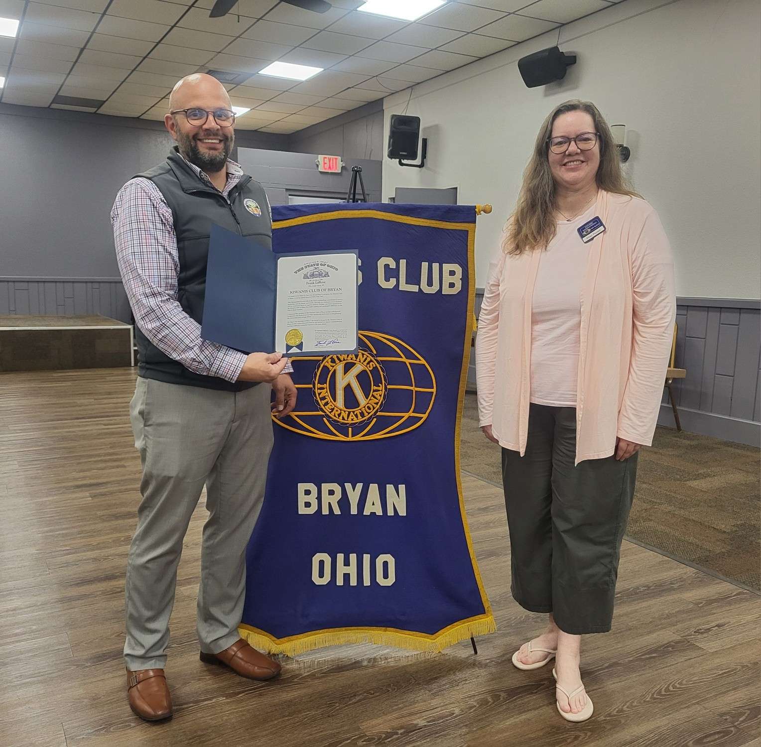 AJ Nowaczyk and Dr. Shay Pursel with the Ohio Secretary of State proclamation in front of the Kiwanis Club of Bryan banner