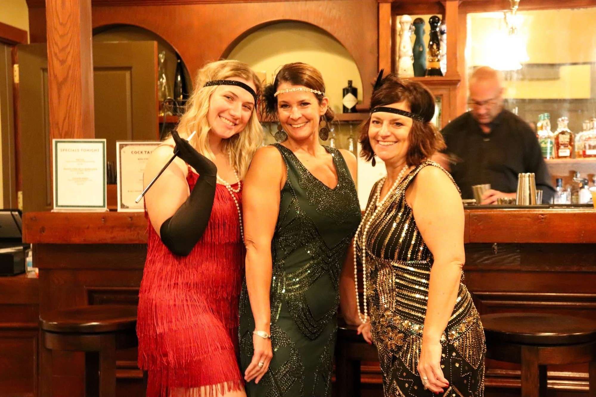 Three guests in 1920s-style dresses and headbands pose at the Speakeasy bar